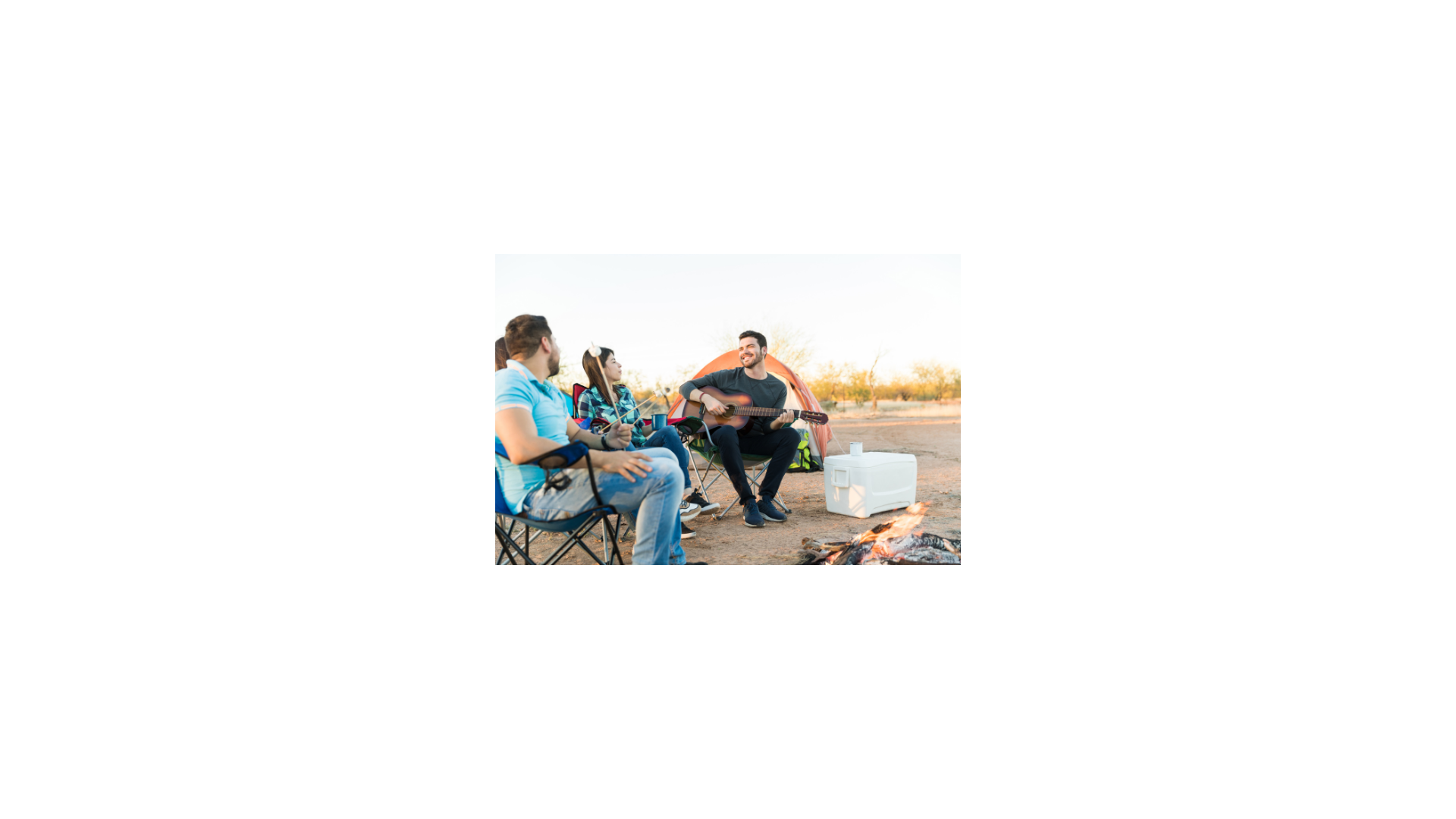 A person playing guitar around a group at a campfire