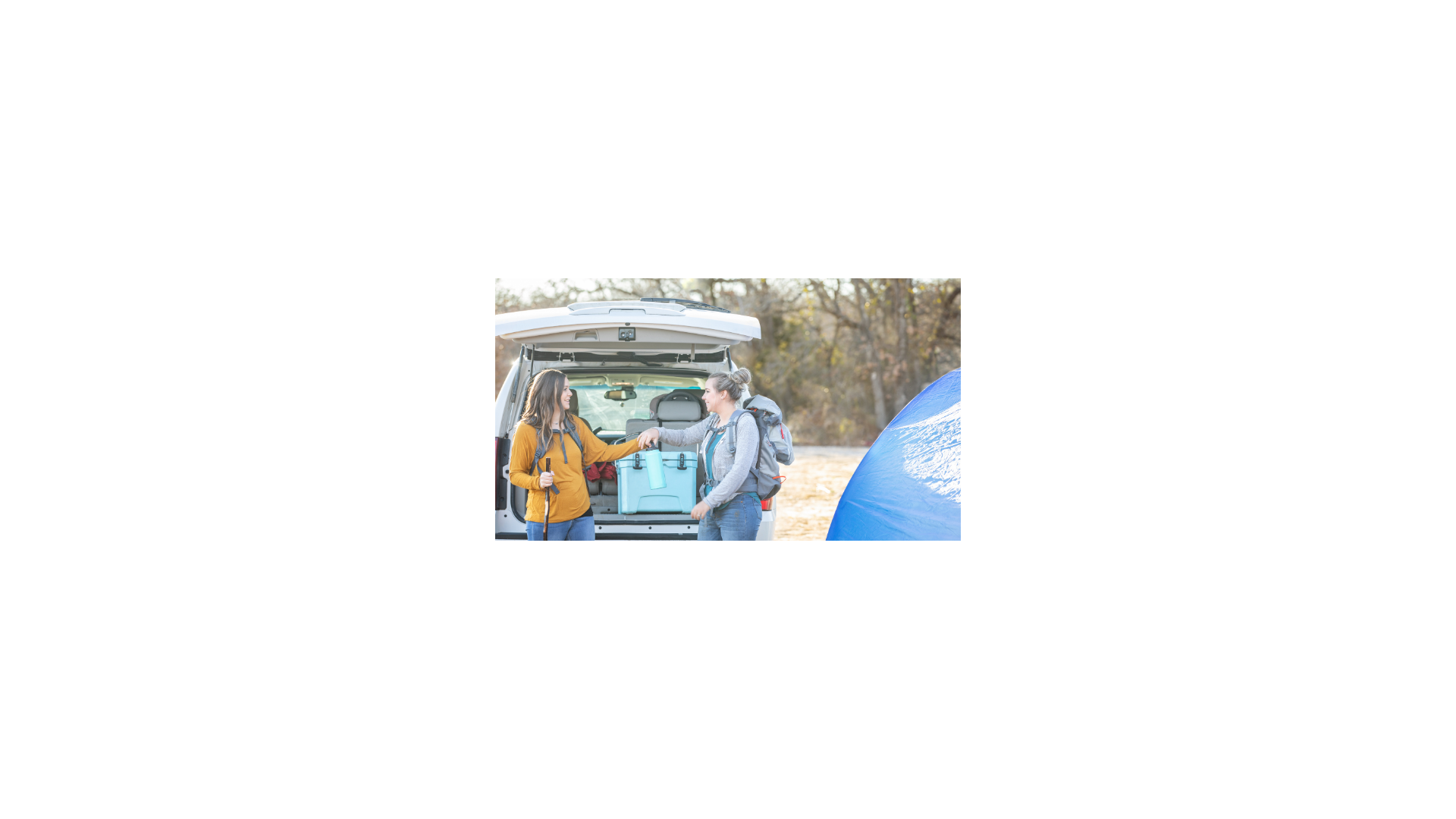 two women holding cooler on back of vehicle