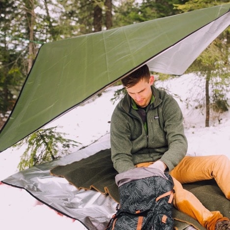 A person sitting on a survival blanket in the snowy forest.