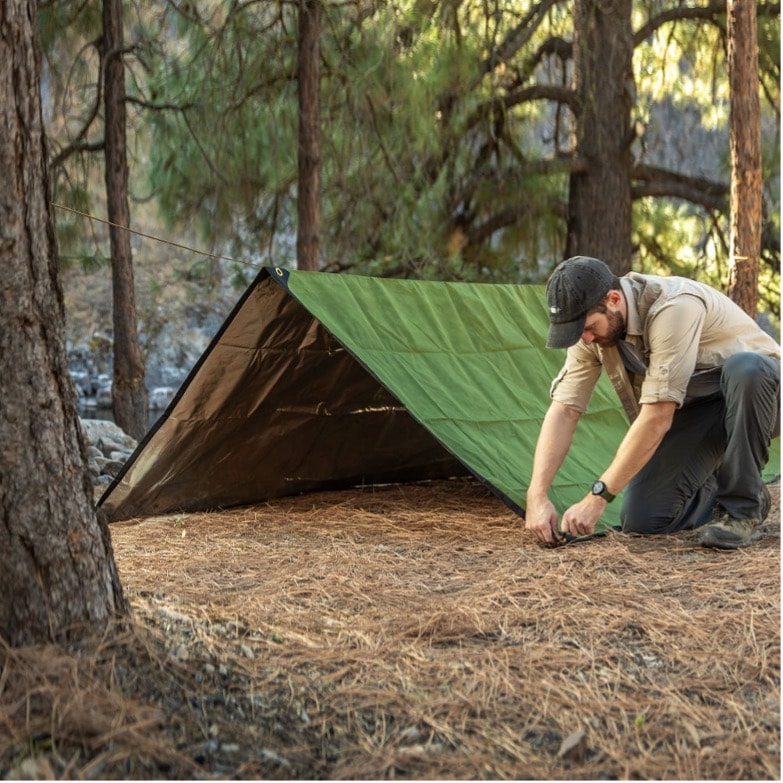 A person kneeling in the woods by a tent